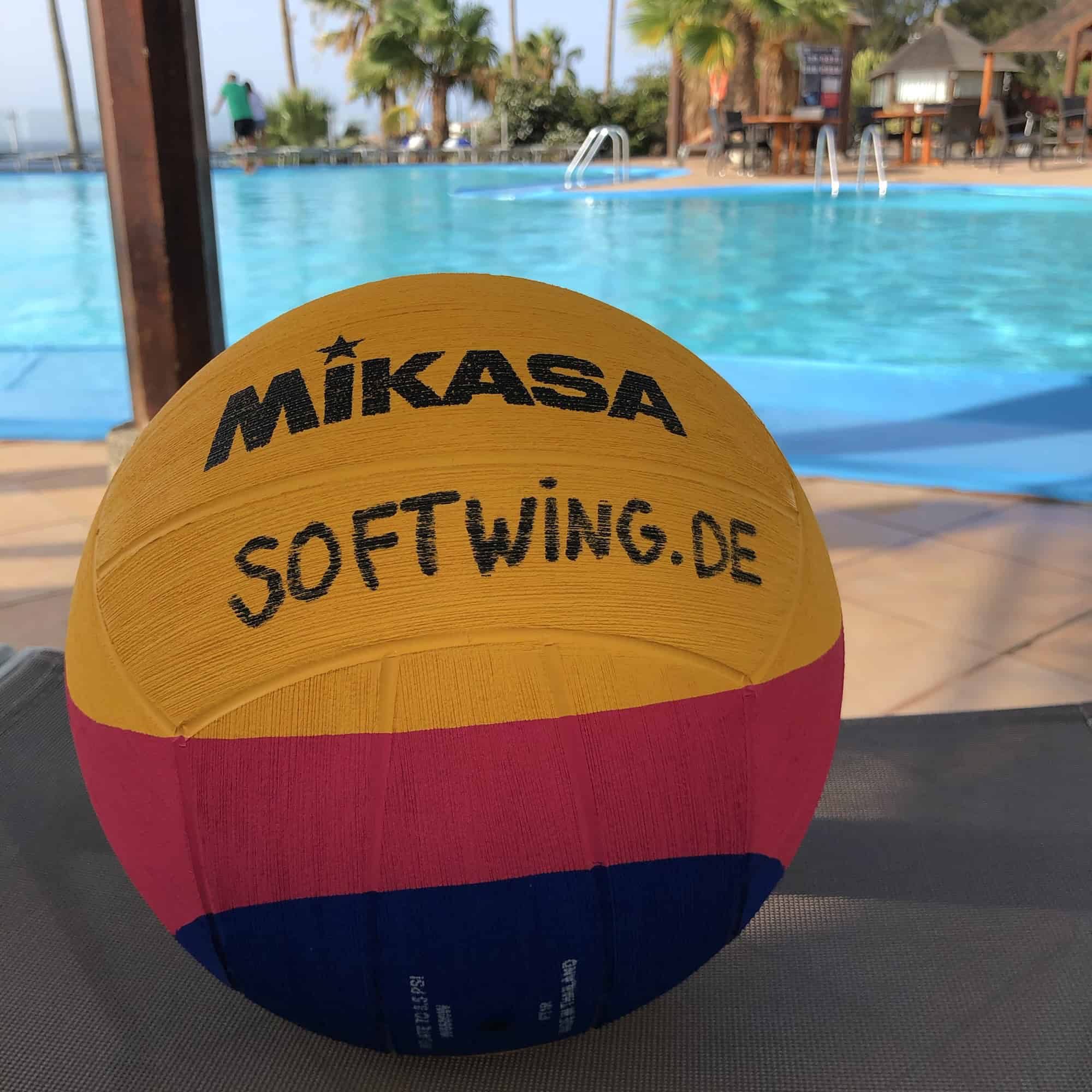 Gelb-bunter Wasserball vor blauem Pool, im Hintrr er grund Palmen eines Urlaubshotels.
