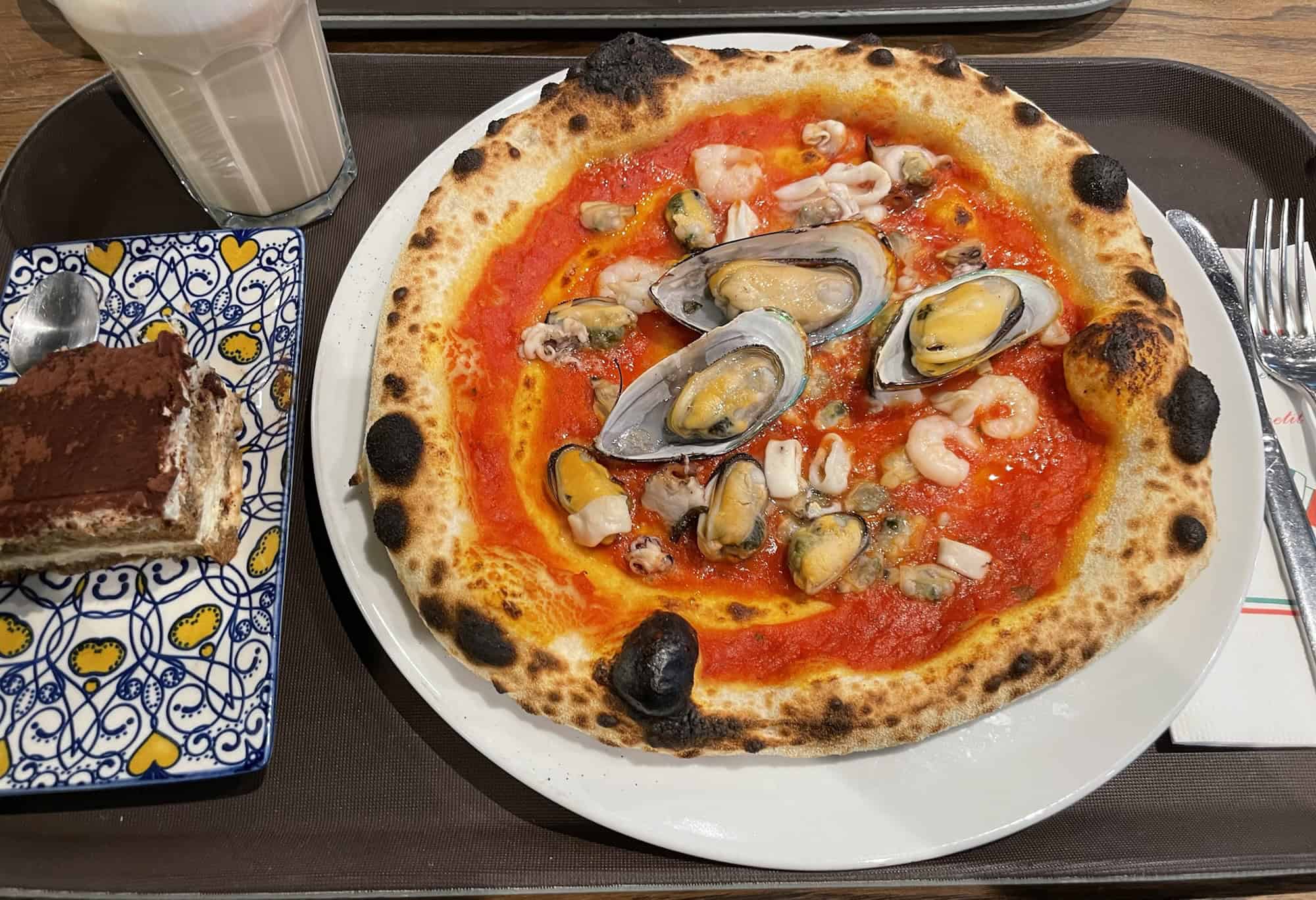 Pizza Frutti de Mare und Tiramisu auf Tablett.