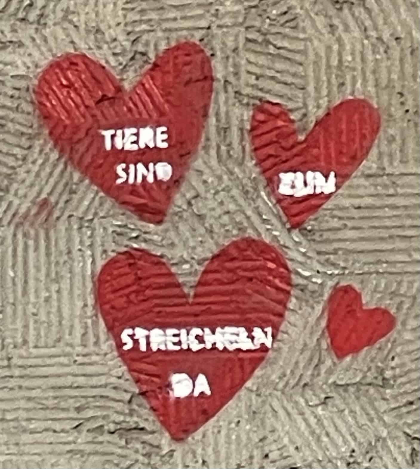 Rote Herzen auf beigee Wand mit Aufschrift: Tiere sind zum Streicheln da.