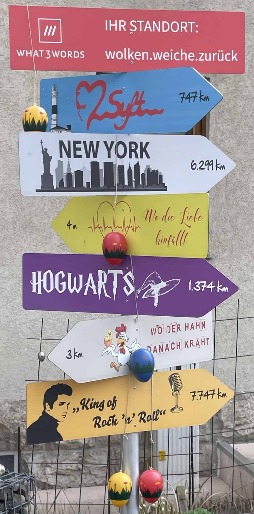 Bunte Schilder mit Orten und Entfernungsangsbrn wie Sylt, Hogwarts, New York oddr kKng of Rock'n Roll.