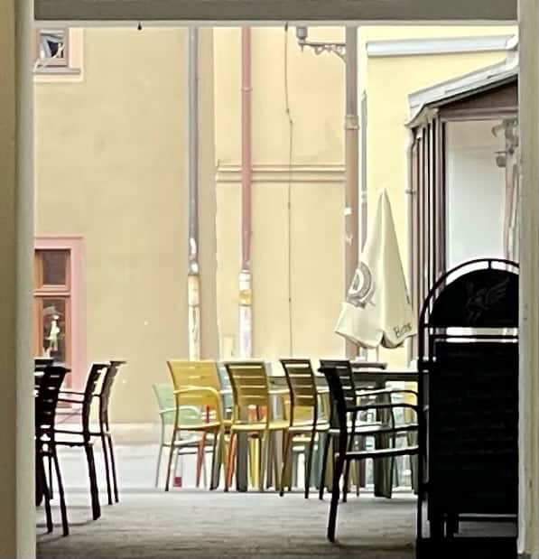 Häuserdurchgang mit Innenhof und Klappstühlen hinten im Hinzergrund., rechts ein Ladengschäft mit Fensterfront