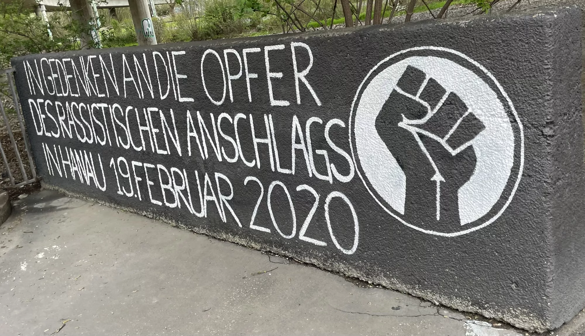 Betonwand mit Aufschrif: IN GEDENKEN AND DIE OPFER OPFER DES RASSISTISCHEN ANSCHLAGS IN HANAU 19. FEBRUAR 2020