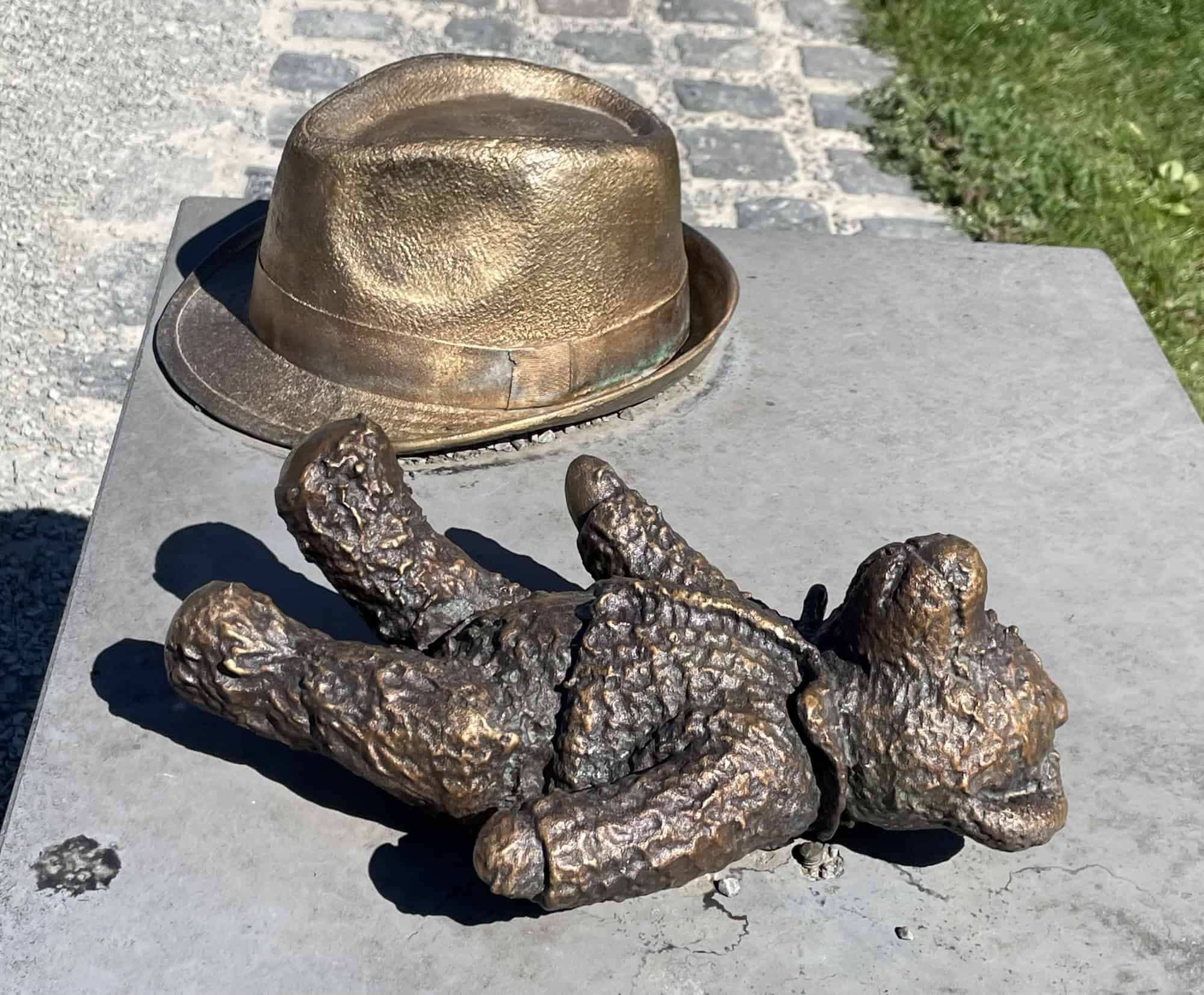 Ein Teddybär und Hut aus Metall auf Steinsitzgelegenheit.