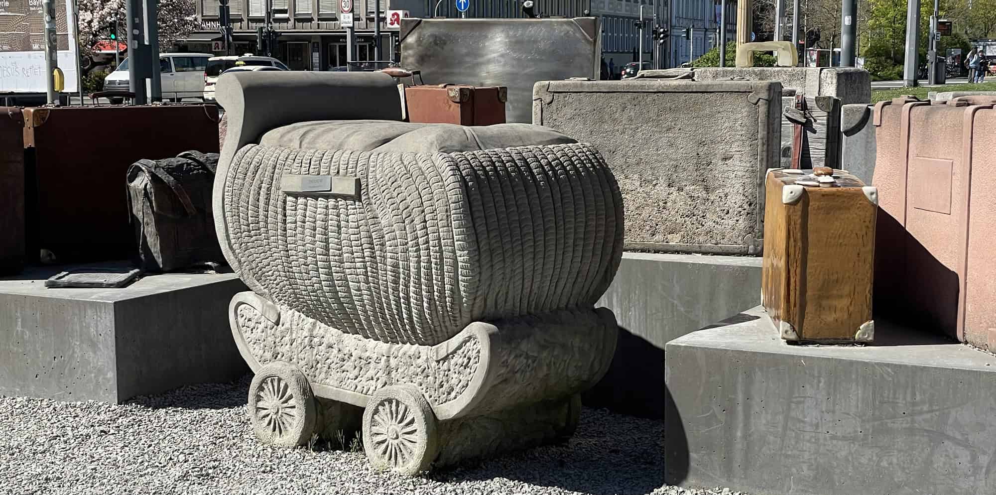 Installation mit Kinderwagen aus Beton vor Kofferfeld.