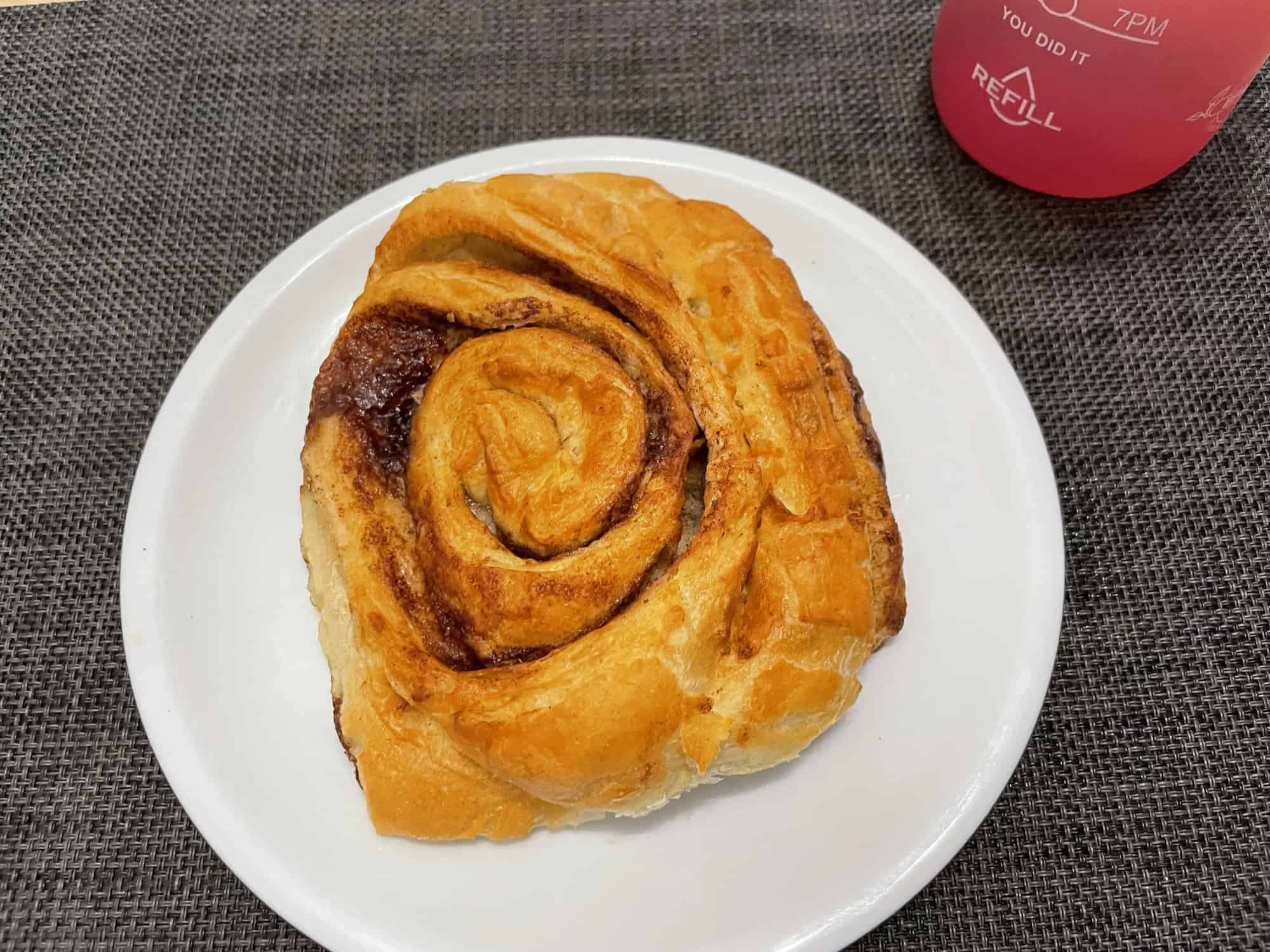 Franzbrötchen auf weißem Teler, antrazitfarbenes Set und rosa Teinkflasche.