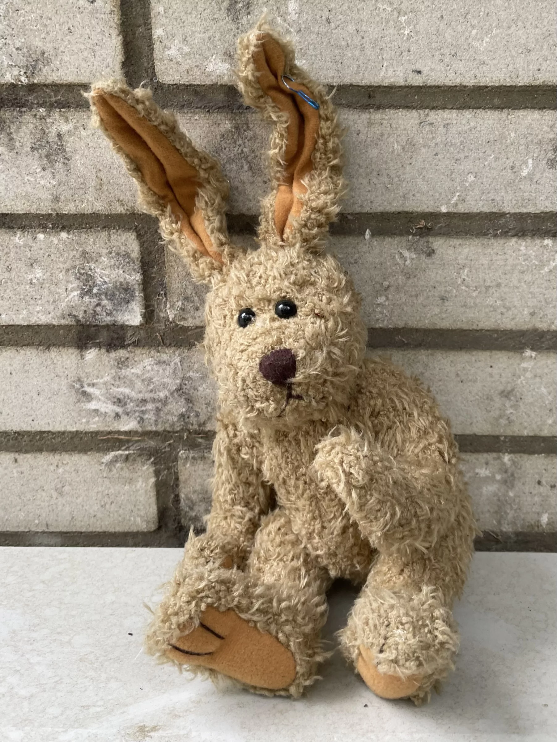 Beiger Stoffhase sitzt an weiße Klinkermauer gelehnt.