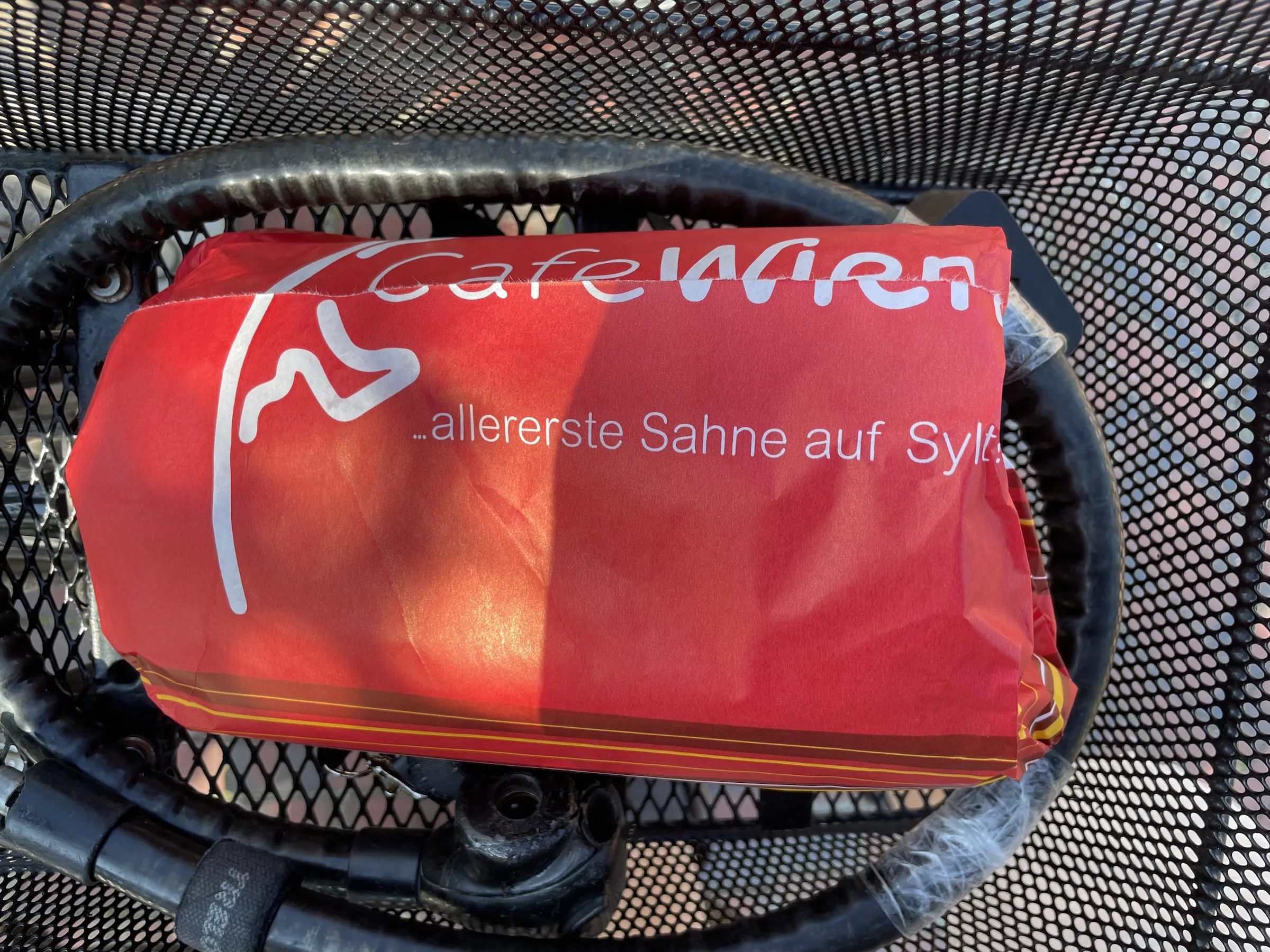 In rotes Papier von Cafe Wien eingeschlsgenes Paket, das in schwarzem Fahhradkorb liegt.