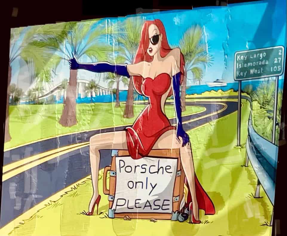 Bild im Comicstyle. Langrothaarige Frau sitzt lazziv im kleinen roten Kleid und lila Langhandschuhe auf ihrem koffer mit dem Schild 'Porsche inly PLEASE'. Hinter ir an der Straße das Schild nach Key Largo und anderen Orten mit Entfernungsangabe. Sie hat den 'Anhalterarm' draußen.