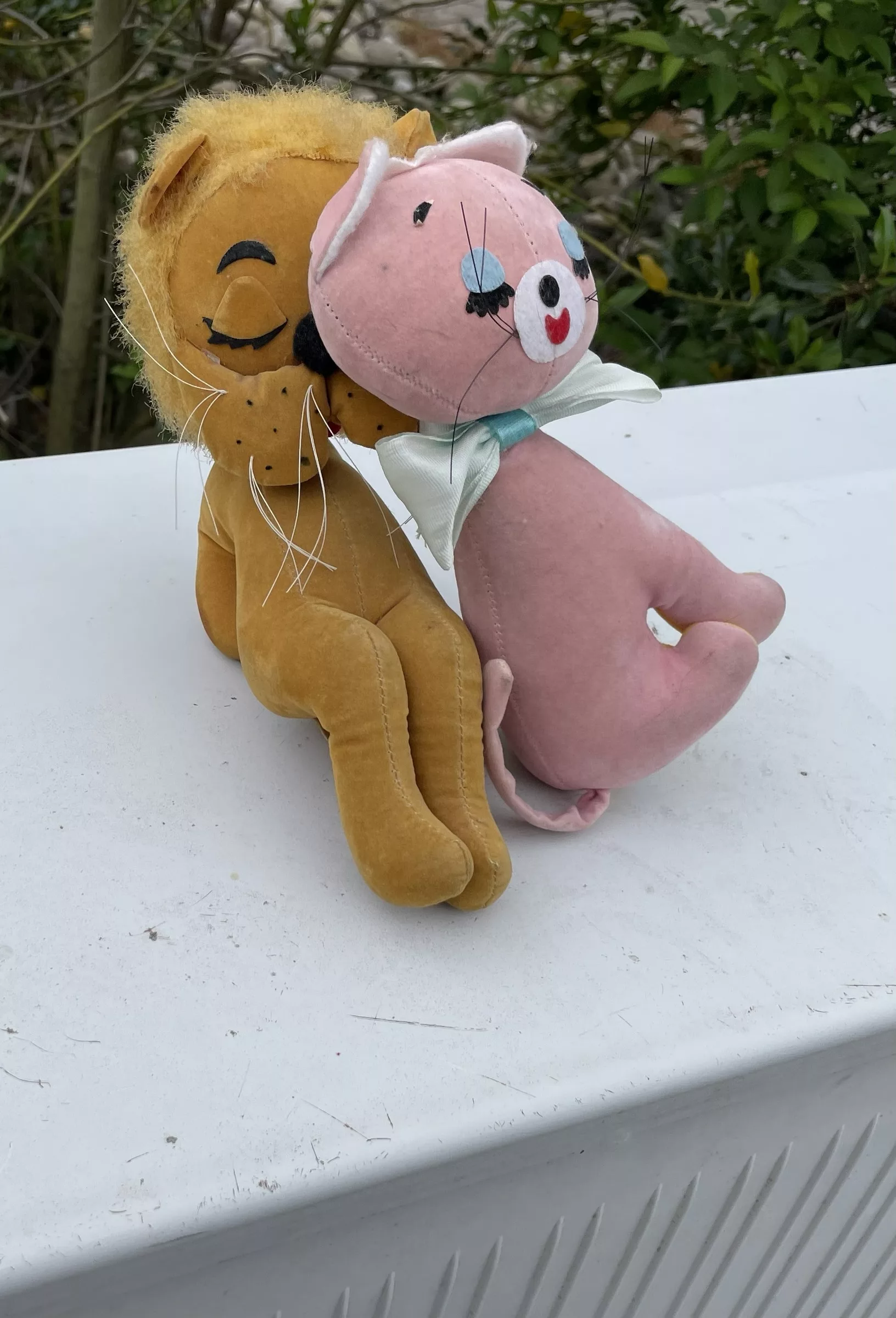 Zwei Kuscheliere, ein Löwe und einr rosa Katze, auf einem grauen Kasten (DSLAM) im Freien.