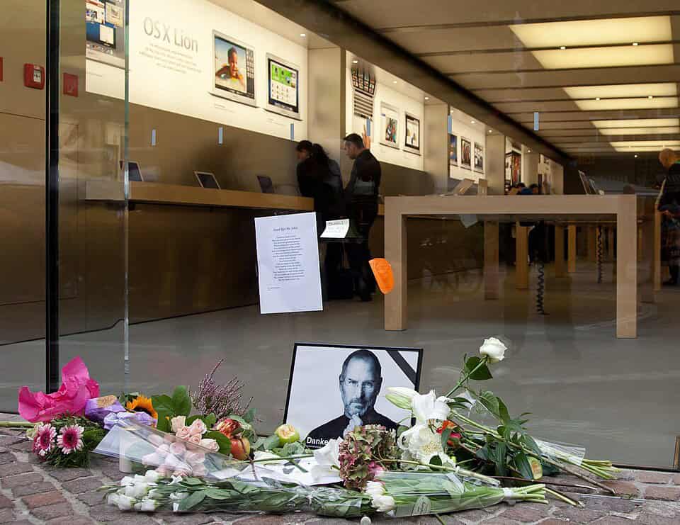 Apple Store Fensterfront mit Blick in den Store. Davor ein Trauerbikd von Steve Jobs mit Blumen und Trauergedicht 'Good Bye Mr. Jobs!'.