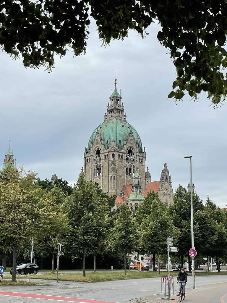 Das Neue Rathaus von Hannover eingerahmt von Bäumen und der Straße davor.