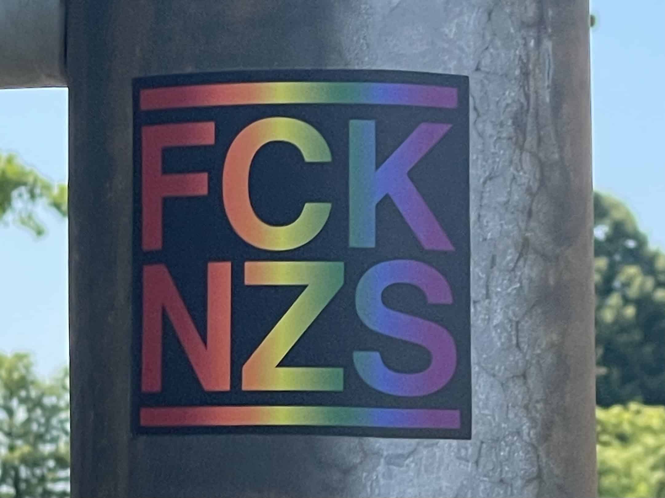 Laternenpfahl mit 'FCK NZS'-Aufkleber in Regenbogenfarbe.