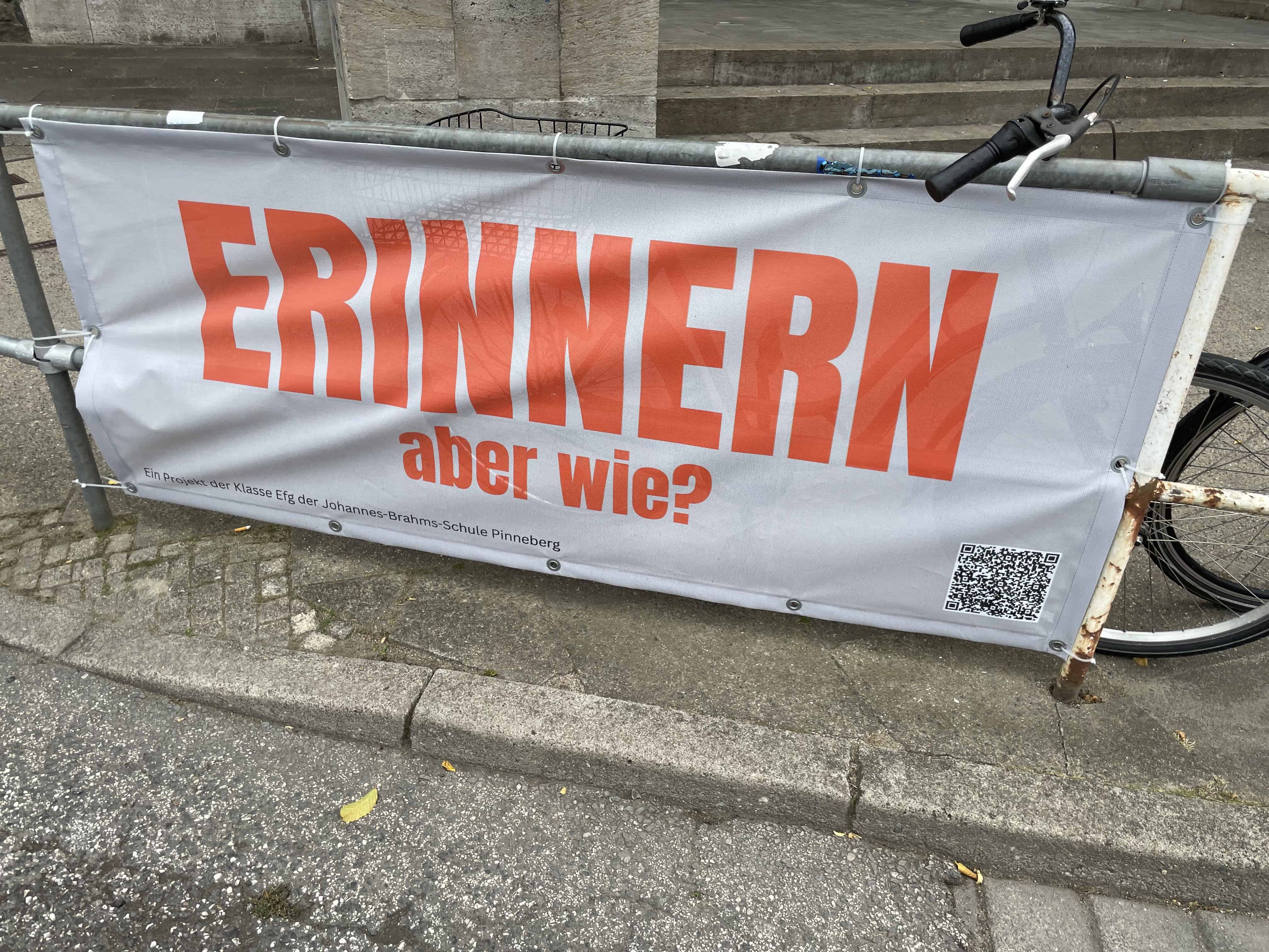 Banner am Gelönder beim Denkmal mit der Aufschrift: ERINNERM aber wie?