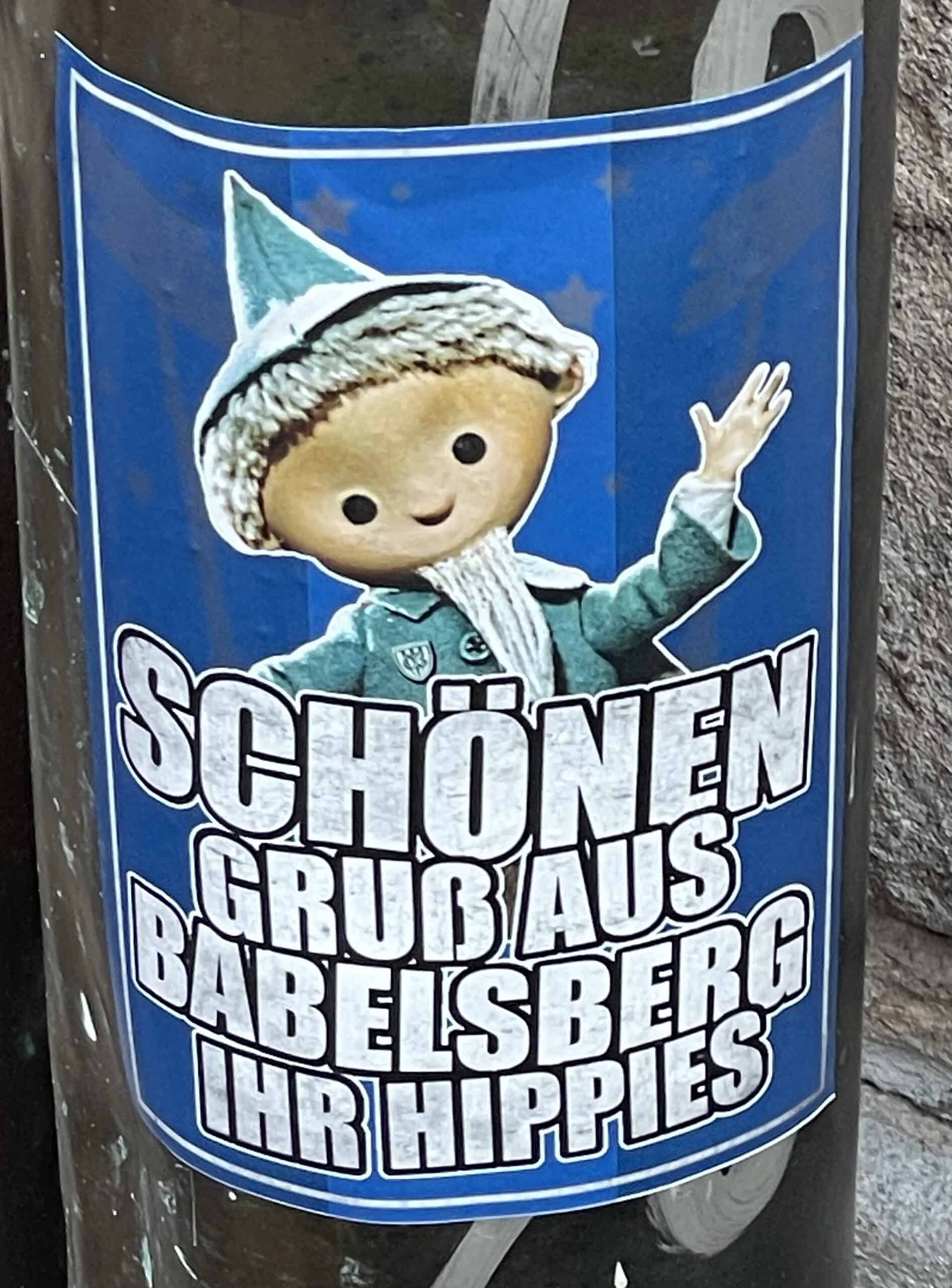 Aufkleber an Regenrohr mit Sandmännchen: SÇHÜNE GRUSS AUS BABELSBERG IHR HIPPIES.