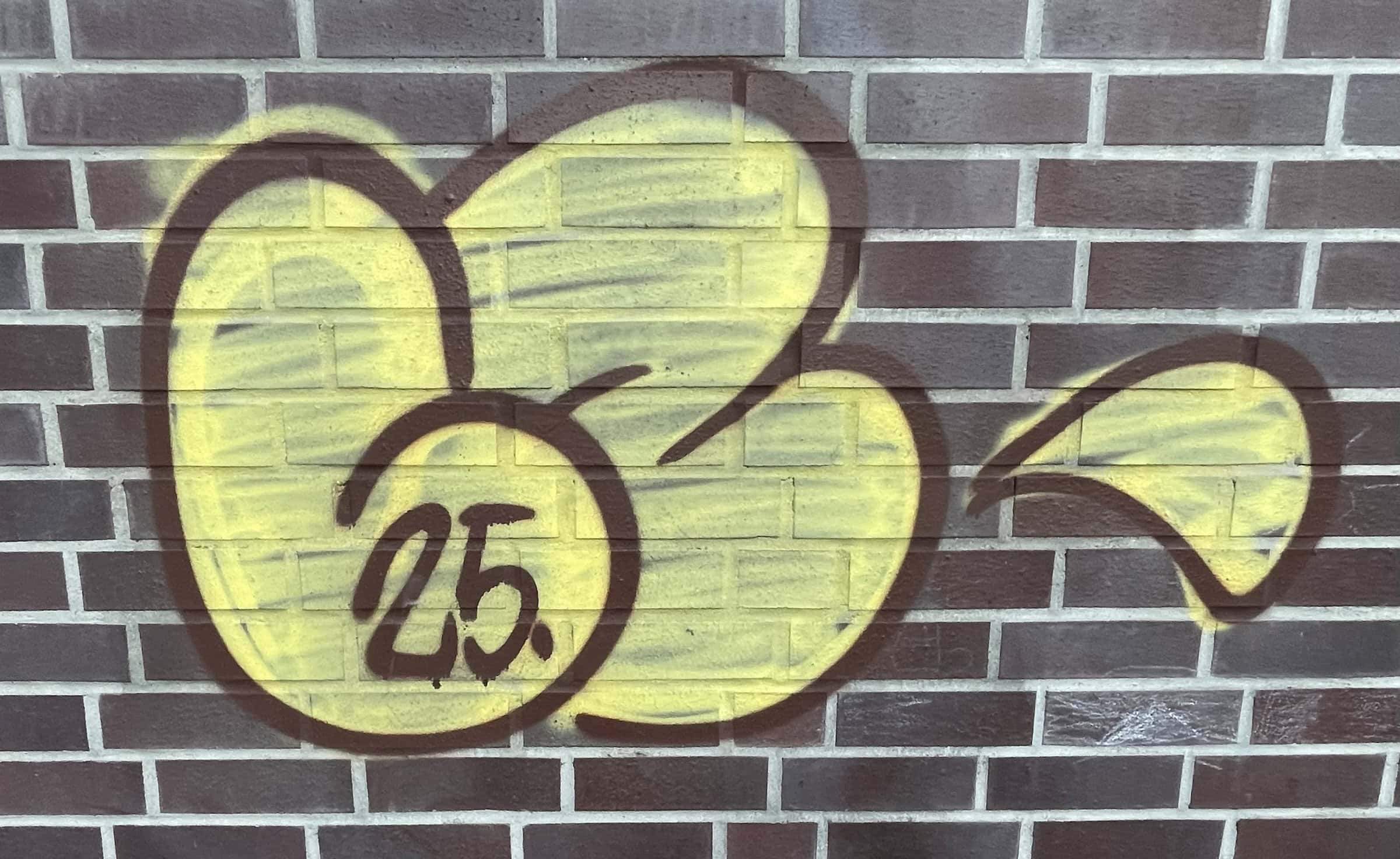 Gelbes Tagging auf dunkelbrauner Klinkerwand.