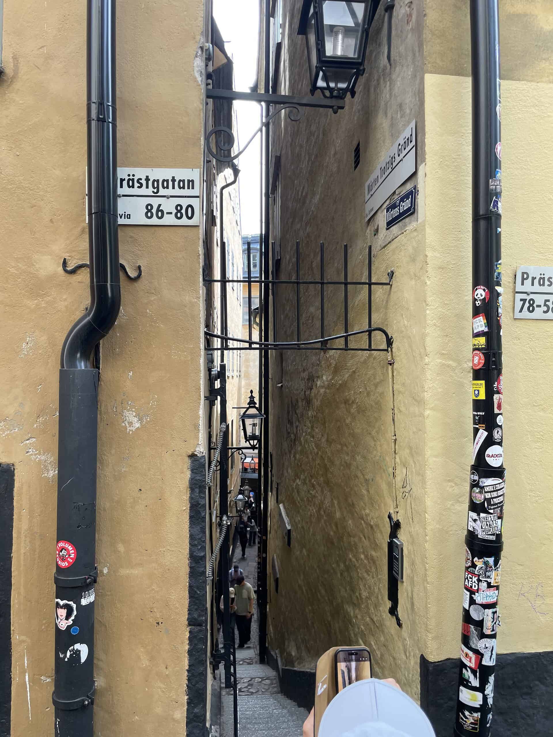 Oberer Eingang zur schmalsten Gasse Stockholms mit links und rechts zwei Regenwasserfallrohren voll mit Aufklebern an den gelben Hauswänden.