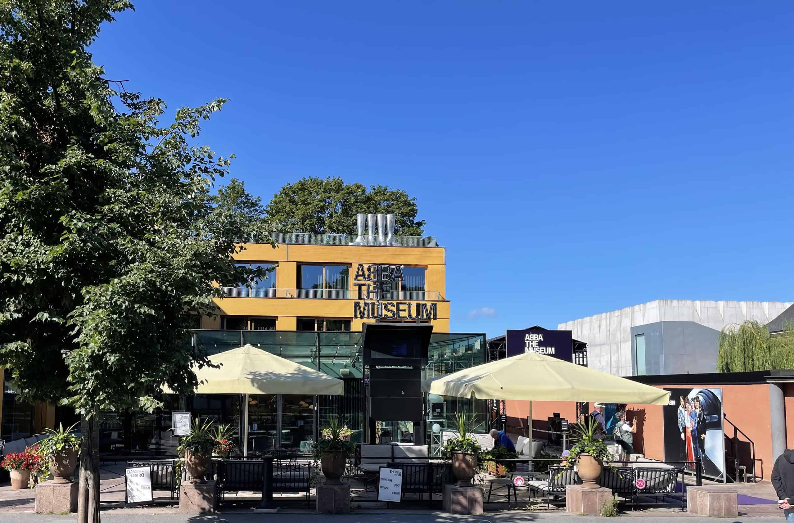 Das ABBA Museumshaus von der Straßenseite mit Sitzgelgehheiten davor und Sonnenschirmen.