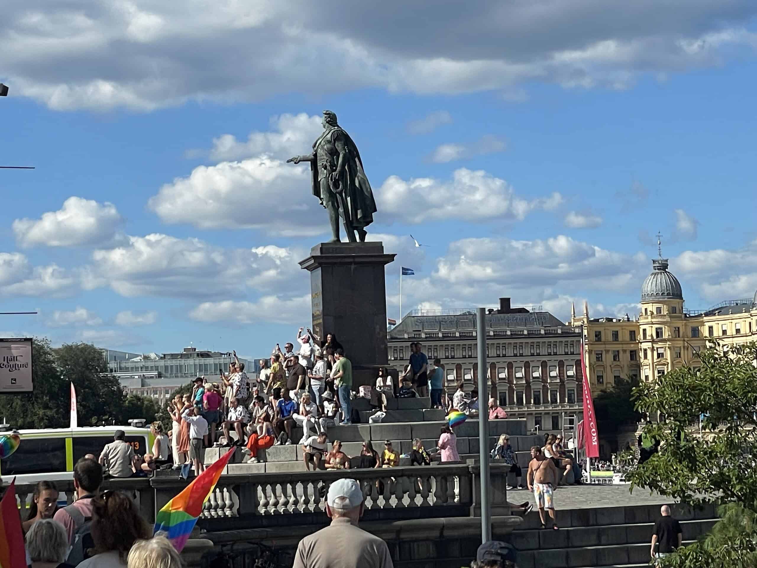 Statue mit historischer Person, darum viele CSD-Teilnehmende.